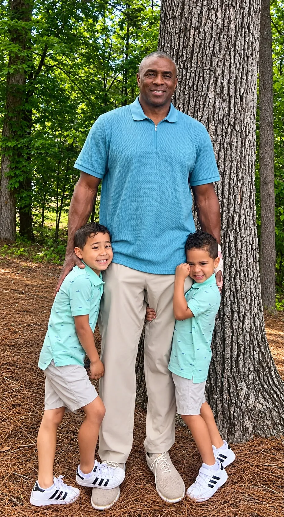 Dwayne Corbitt smiling with two young boys from his family, standing by a tree outdoors